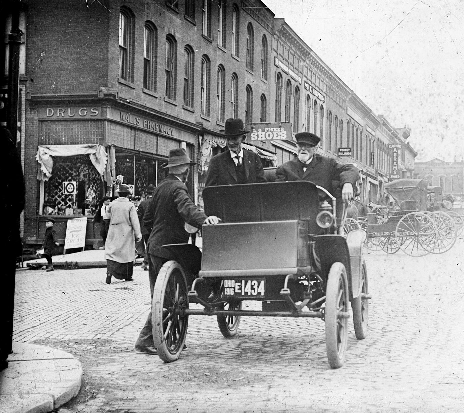 Historic photograph of Medina Public Square around 1916, with a Baker Electric automobile in view. The square is surrounded by brick storefronts.