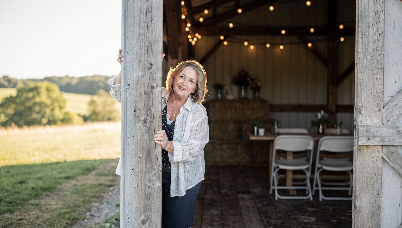 A mother of the bride in her early 60s standing in the doorway of a restored Medina County barn wedding venue, hand on the door frame.