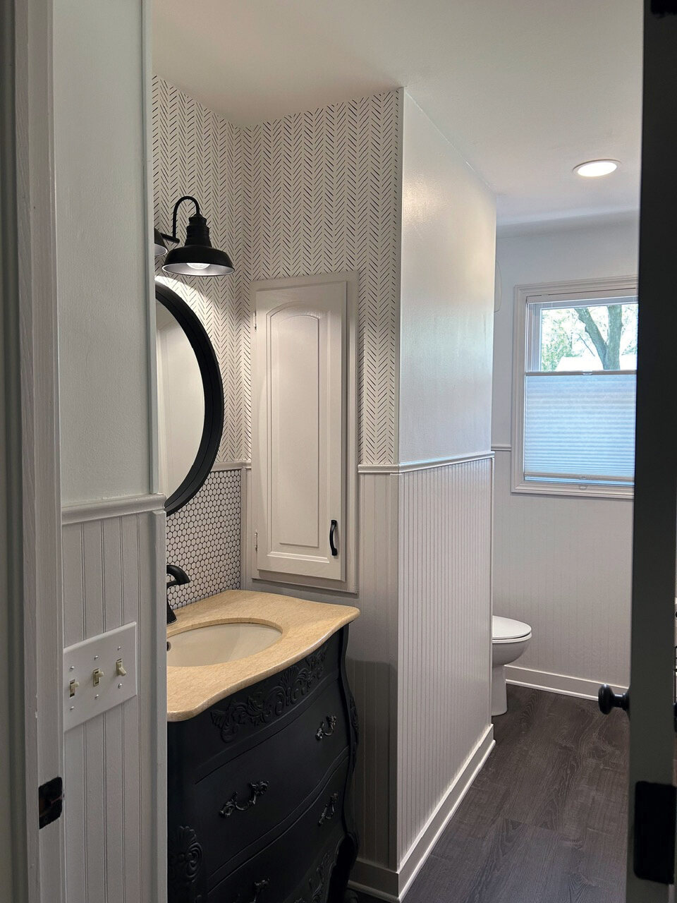 Lower-level bath with a dark vanity and round mirror
