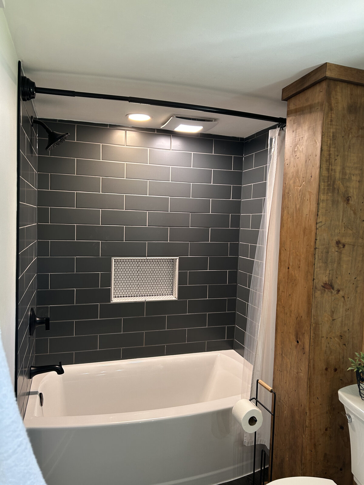 Tub and shower with dark subway tile and a wood surround
